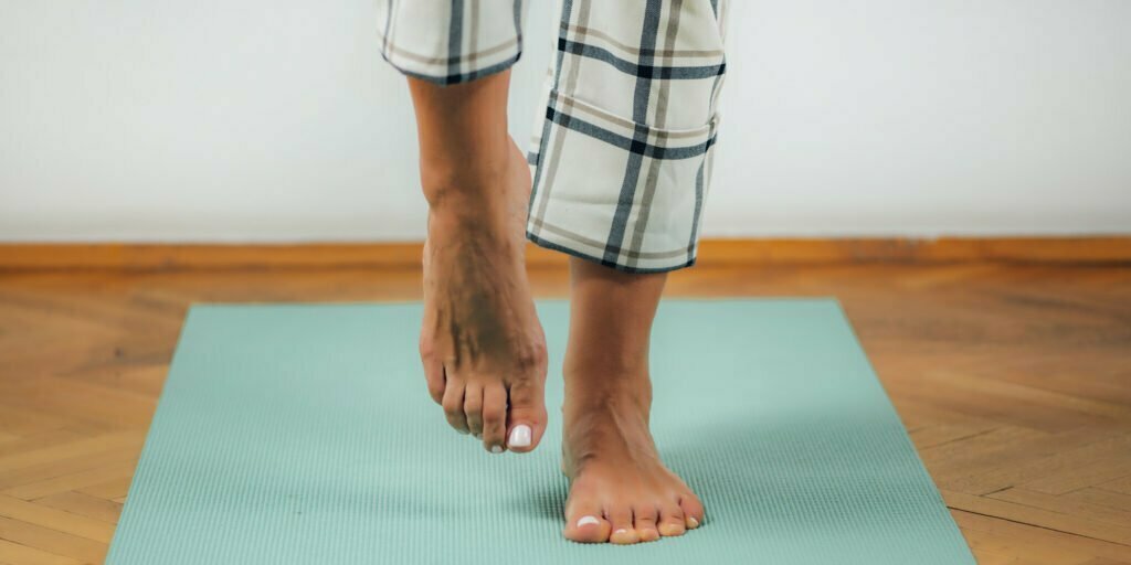Utsnitt av føttene til en dame som står på ett ben på en treningsmatte