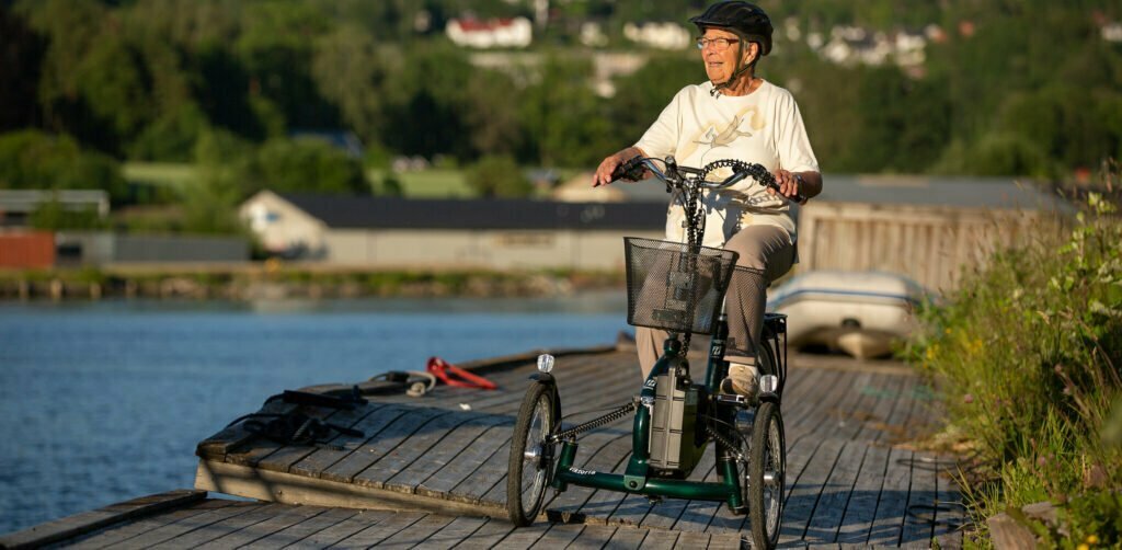 En fornøyd eldre dame sykler på sin trehjulssykkel med to hjul foran på brygga i Skien.