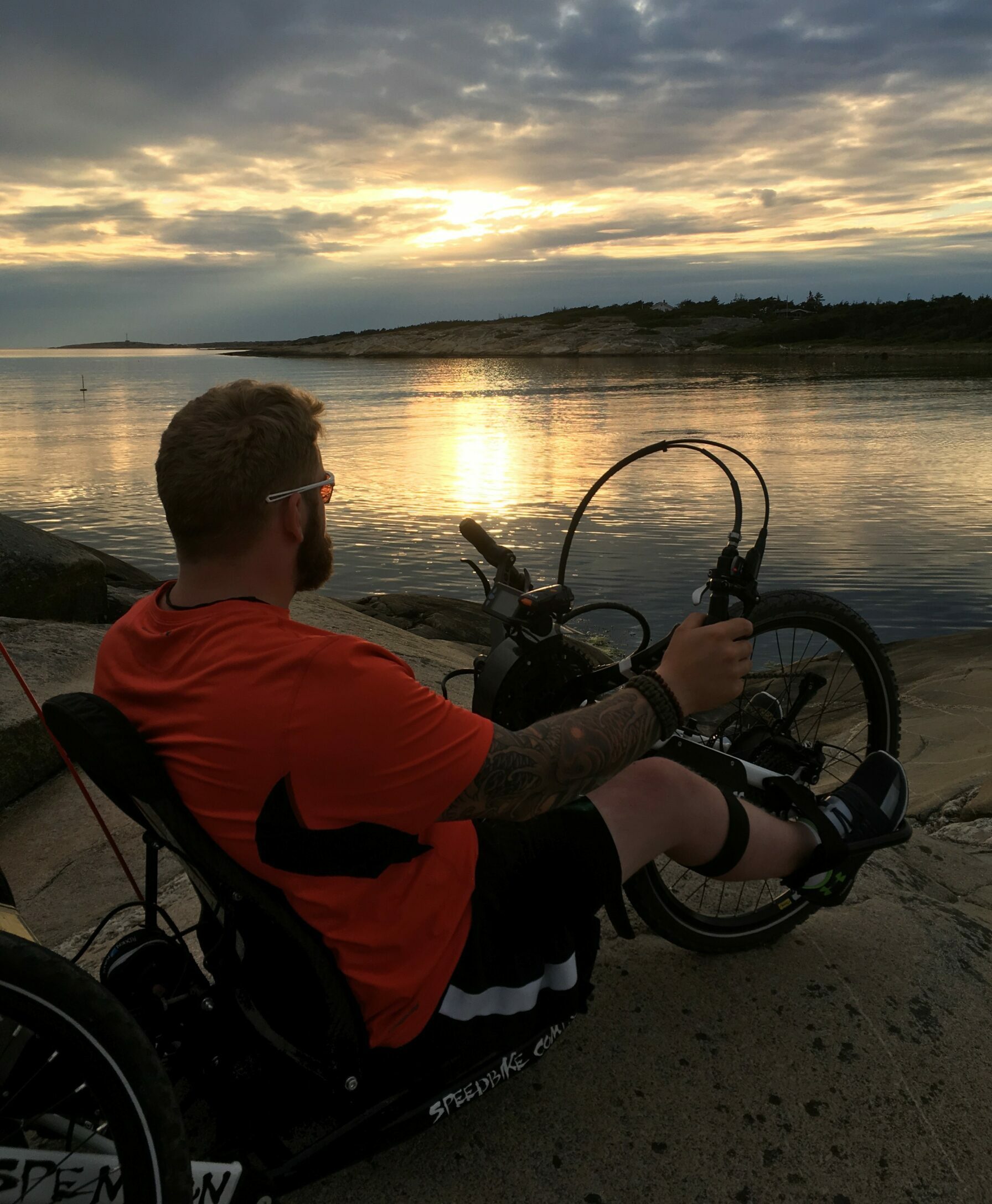 Mann på håndsykkel ved sjøen i solnedgang. Foto.