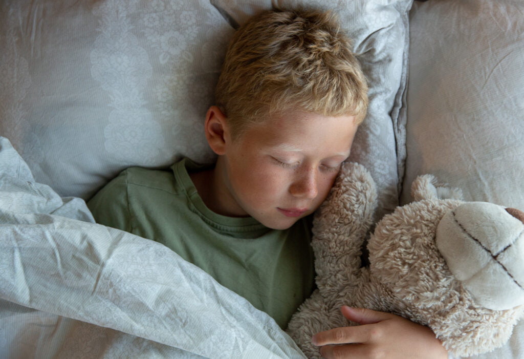 Gutt sover i sengen sammen med bamsen sin