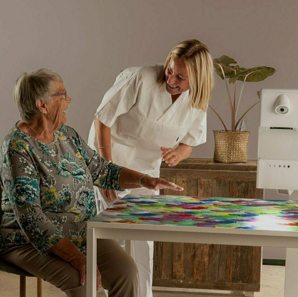 Eldre dame og sykepleier gleder seg over levende bilder og spill